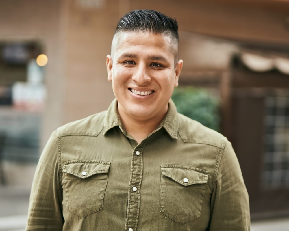 A man in a green shirt standing in front of a building smiles at the camera.