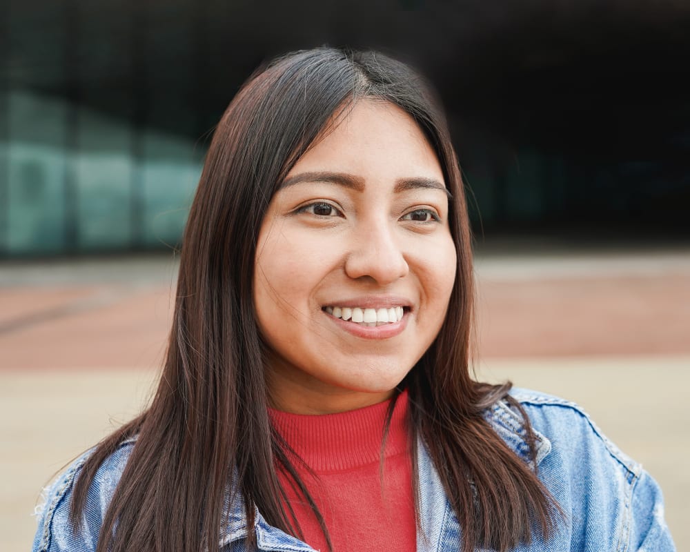 Smiling Indigenous woman wearing a red shirt and a jean jacket.