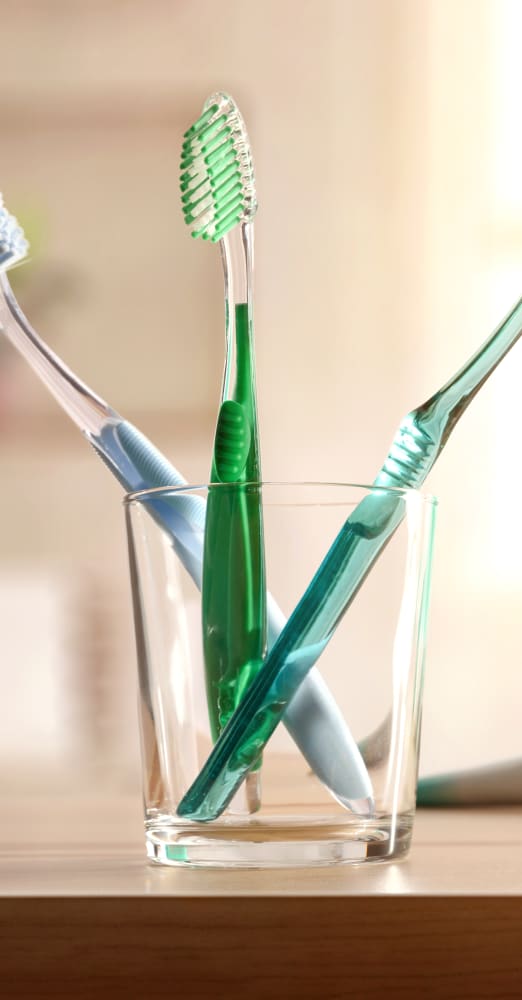 Three green tooth brushes sitting upright in a clear glass cup.