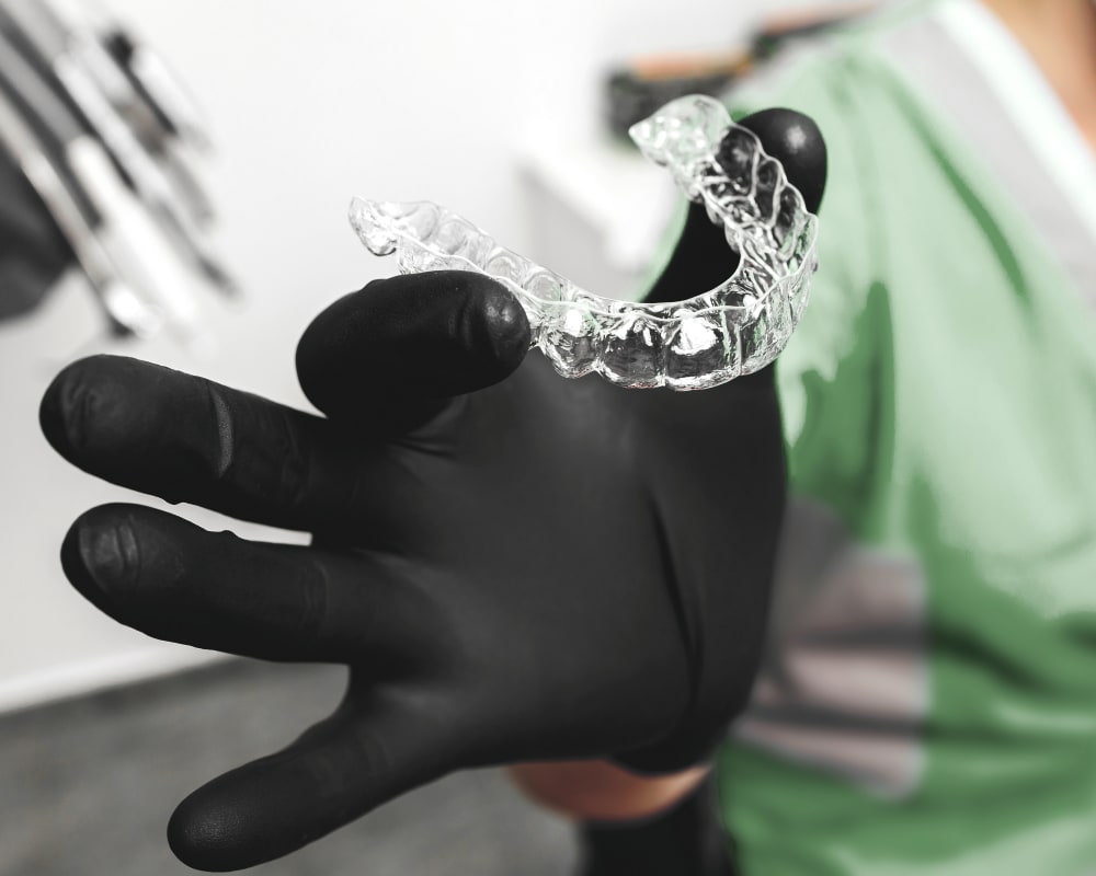 A dental professional with gloves on holding an Invisalign clear aligner.
